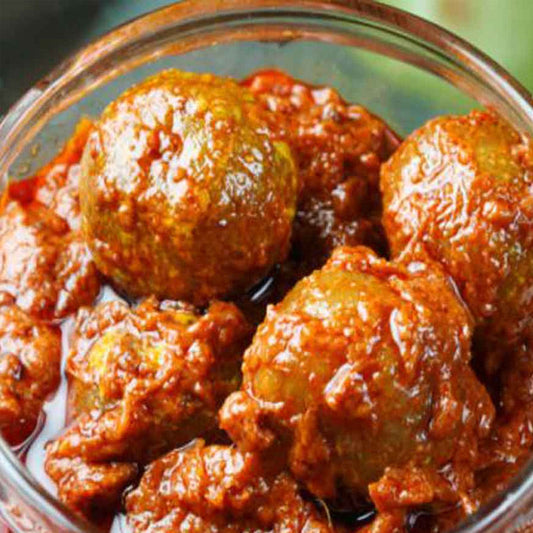 A glass bowl filled with spicy amla pickle, submerged in a red-colored spicy sauce.