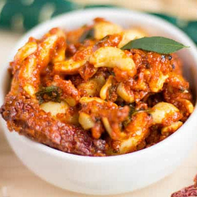 Spicy and tangy Cashew Pickle (Kaju Pickle) in a bowl with curry leaves, handcrafted by Athithi Gruha Foods.